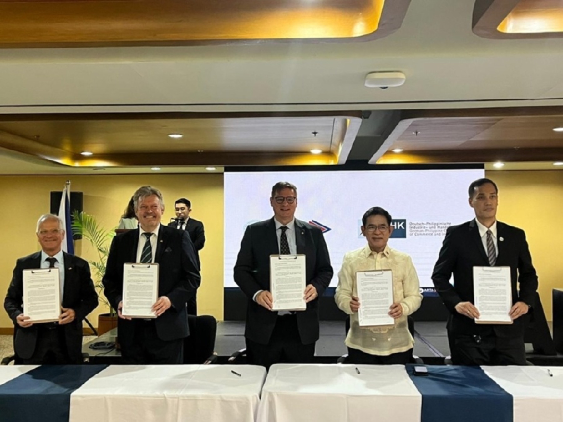 Five signatories holding signed memorandum folders, under the bilingual chamber lockup